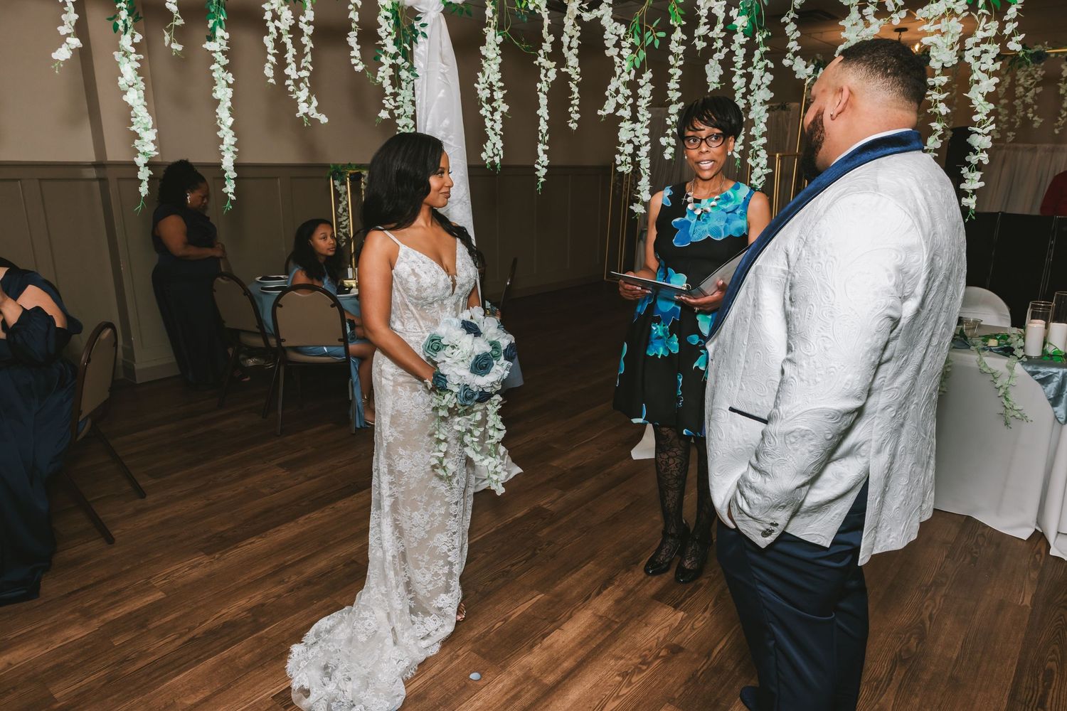 Bride and groom exchange vows during an elegant indoor wedding ceremony with greenery decorations.