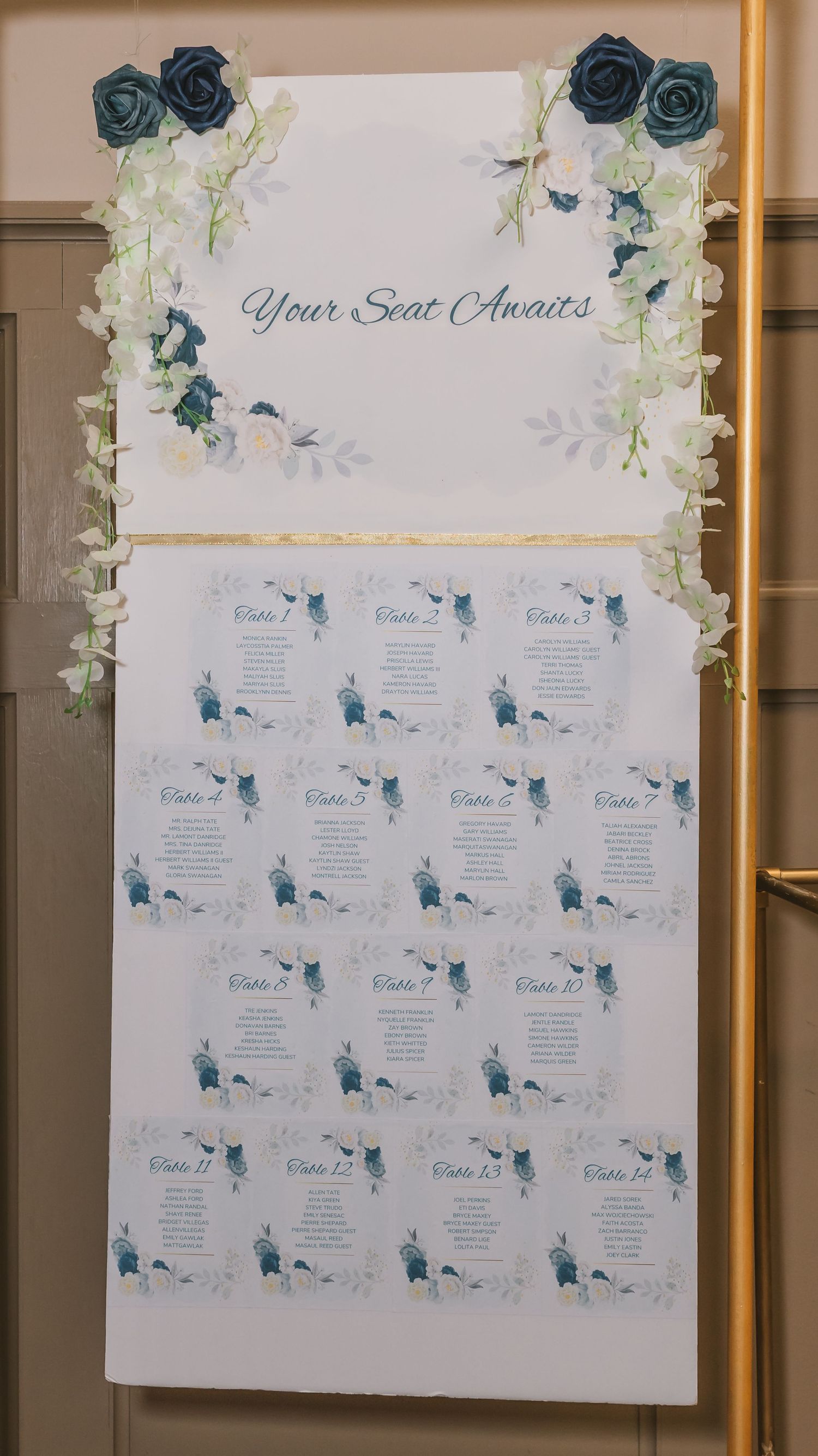 Wedding seating chart display reading Your Seat Awaits decorated with navy blue roses and white floral accents.