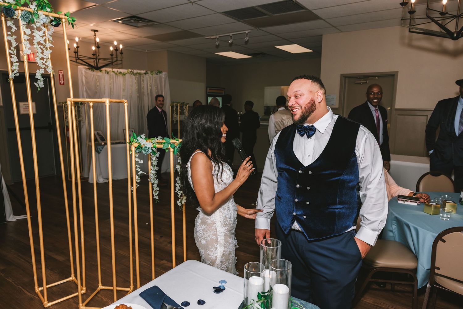 Bride and groom laughing together near gold geometric arch display at wedding reception.