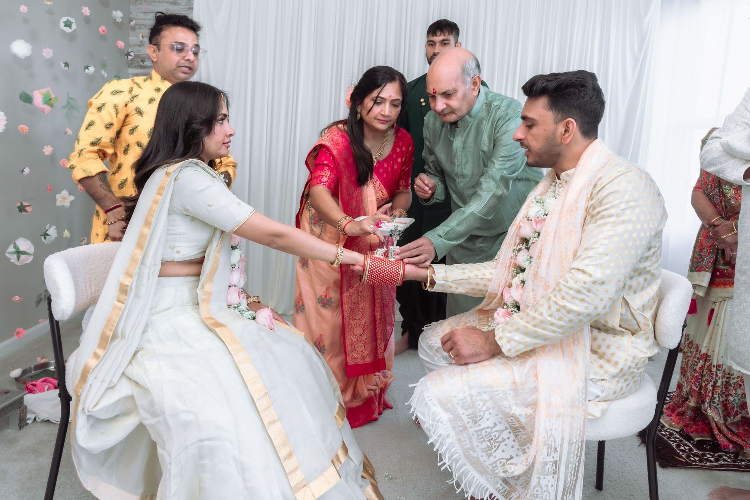 Indian wedding ceremony with family members blessing bride in white lehenga and groom in cream sherwani.