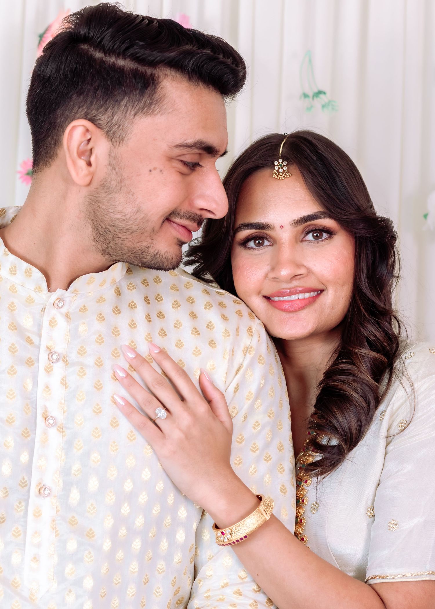 Indian couple in white traditional outfits share a romantic close moment at a festive celebration.