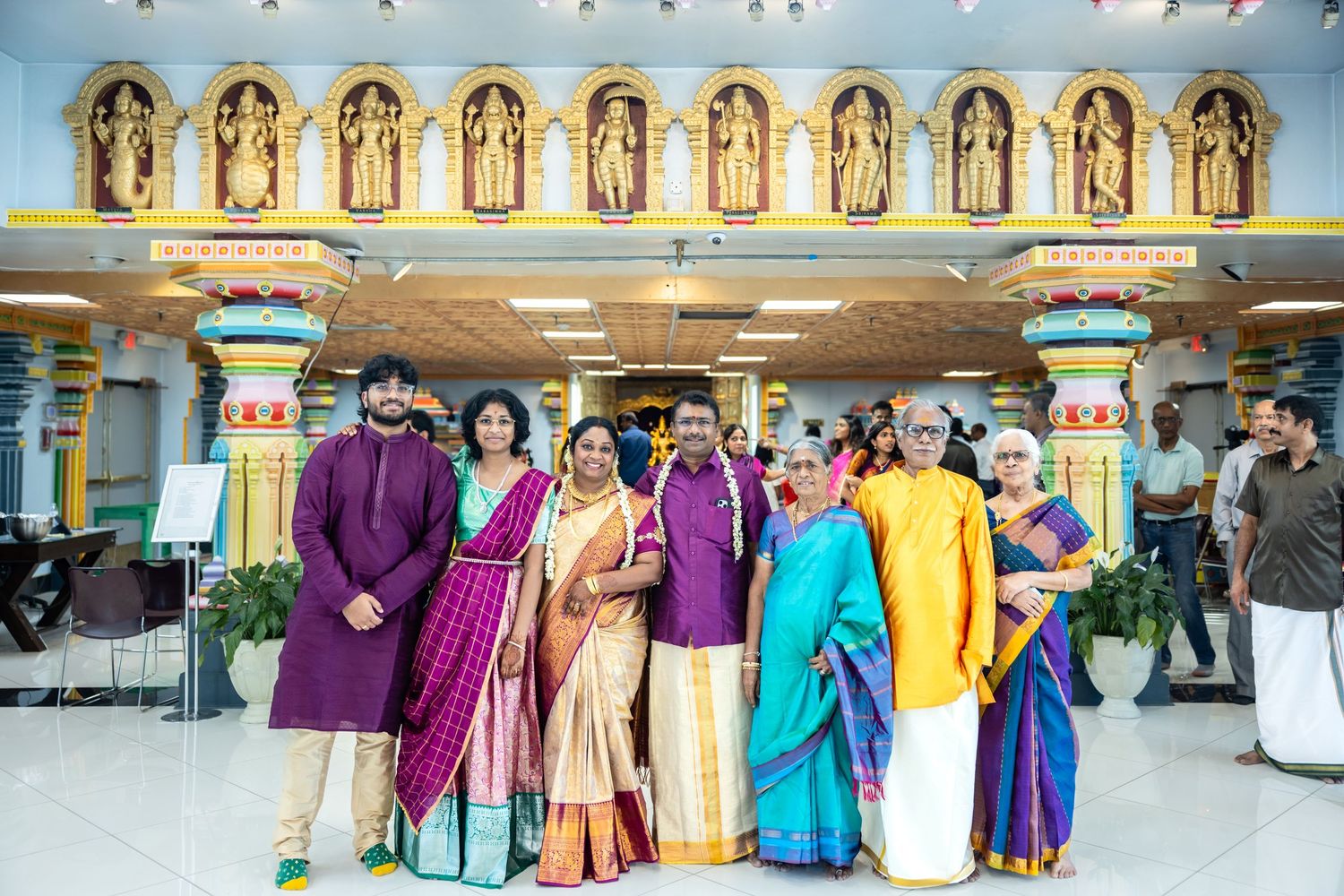 South Indian family in traditional silk attire posing together outside a decorated Hindu temple.