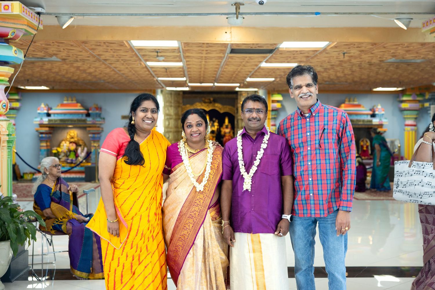 Four smiling people wearing colorful traditional Indian clothing posing together inside a Hindu temple.