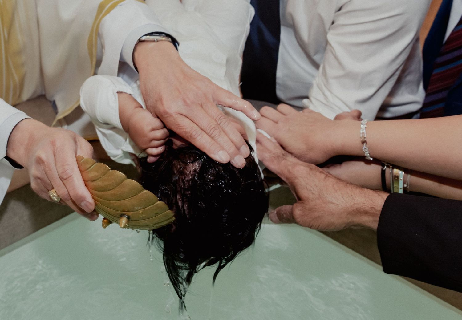 Close-up of baby baptism water blessing with multiple hands during christening ceremony.
