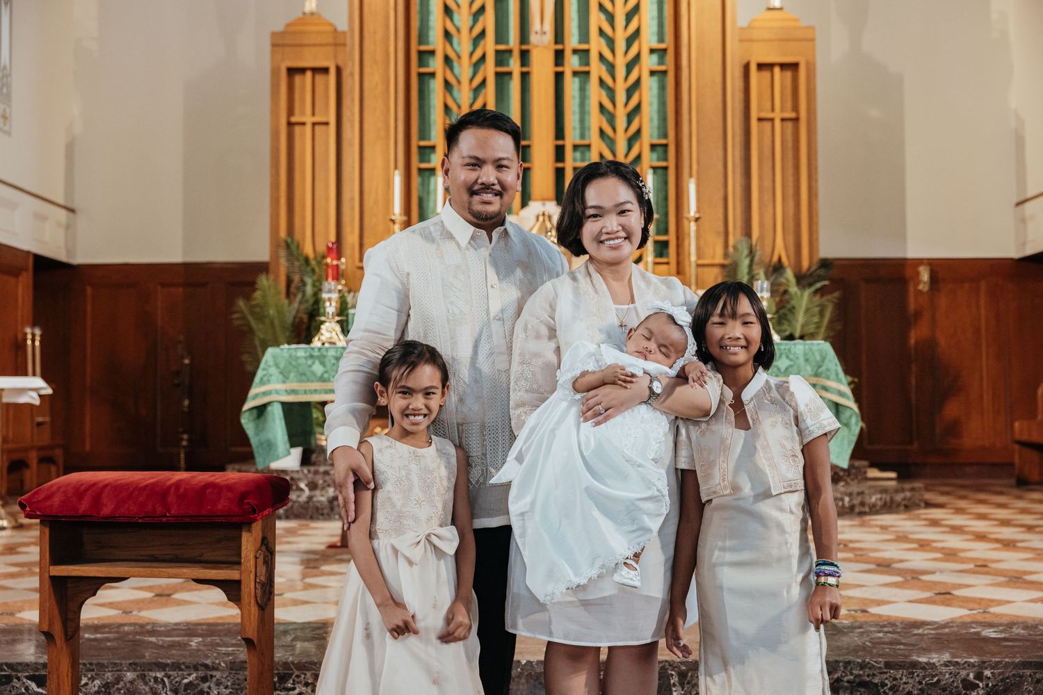 Filipino family of five in white attire poses before church altar at baptism.