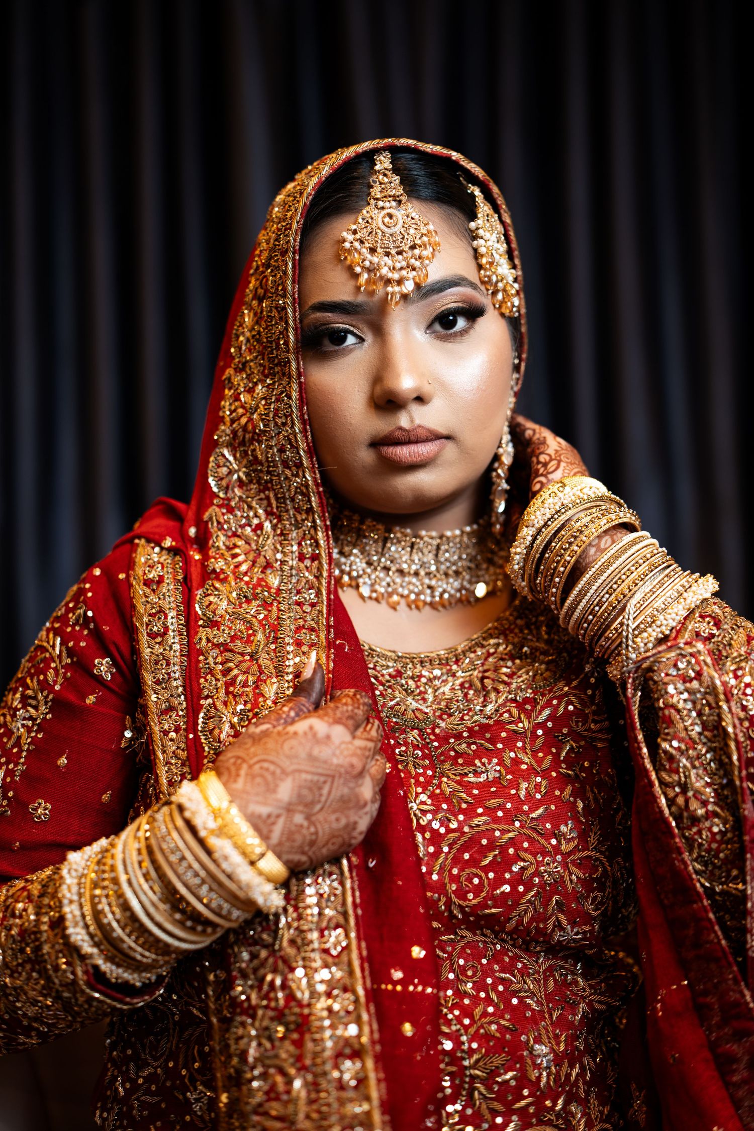 Indian bride in traditional red and gold bridal lehenga with ornate gold jewelry and maang tikka.