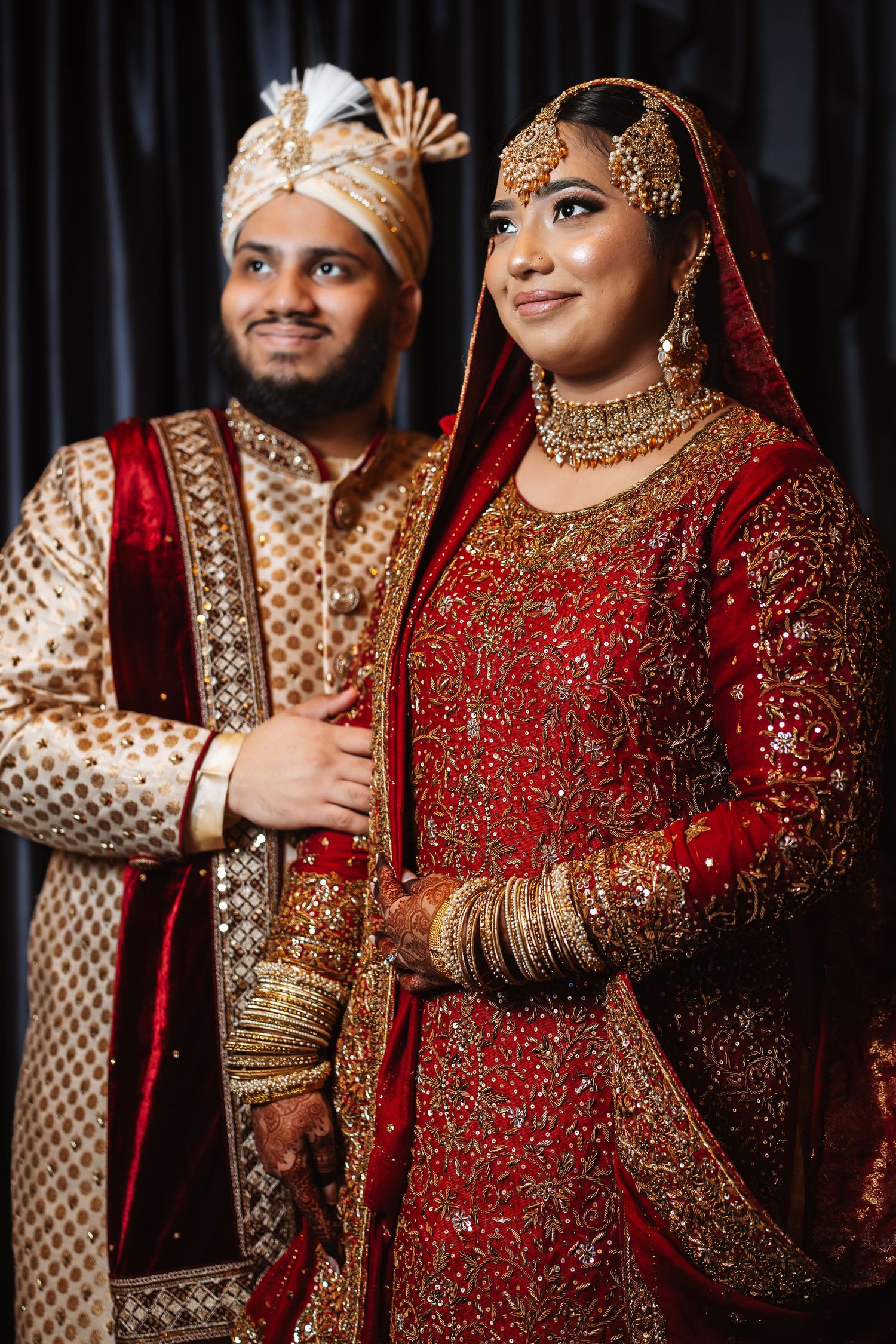 South Asian bride and groom posing together in traditional red and gold bridal attire and sherwani.