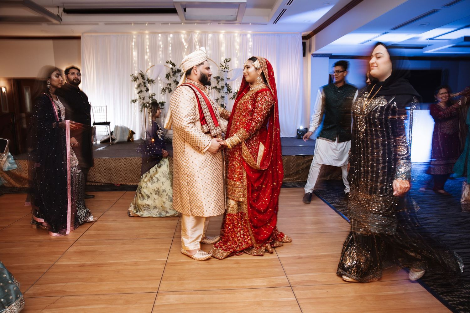 Indian wedding couple in traditional attire exchange vows surrounded by guests in elegant venue.
