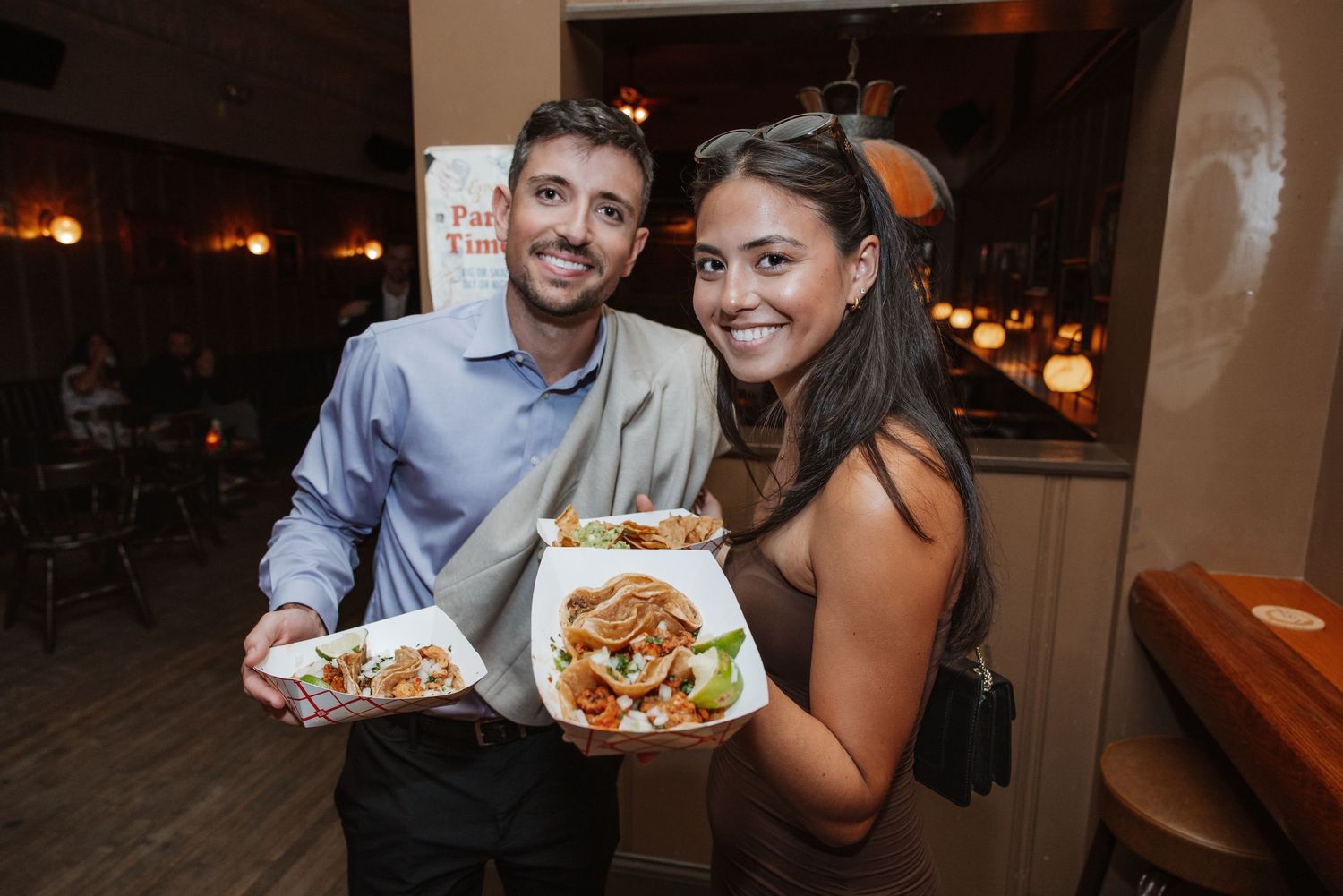 Smiling couple posing with food containers at a warm, dimly lit restaurant.