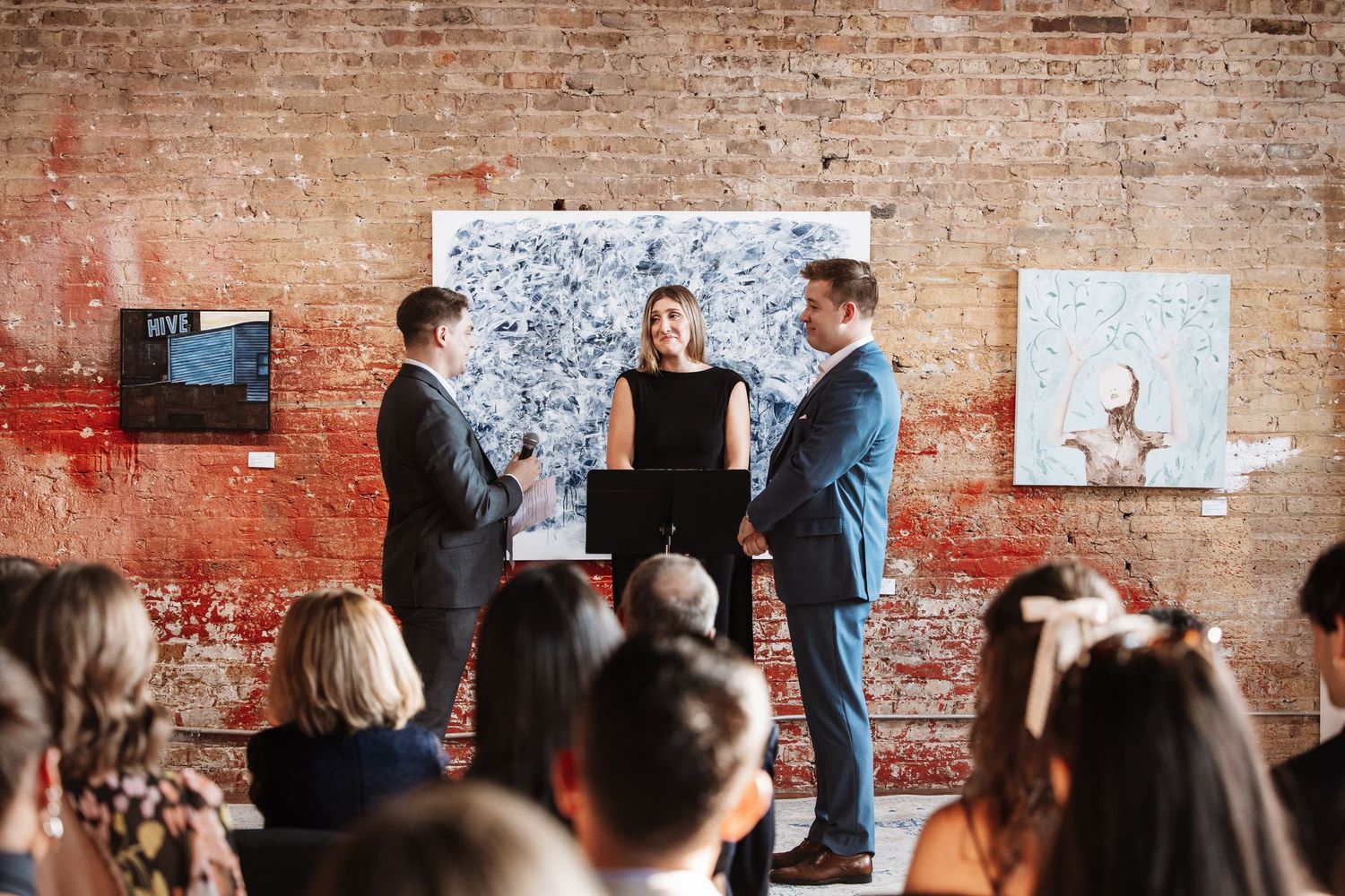 Wedding ceremony with couple exchanging vows before guests in a rustic brick art gallery.