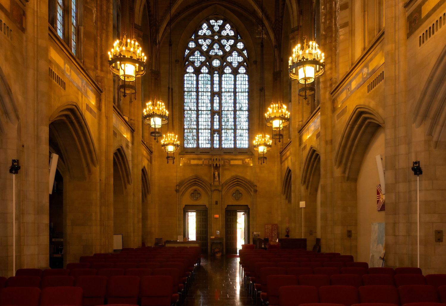 Stunning Gothic church interior with red pews, ornate chandeliers, and colorful stained glass window.