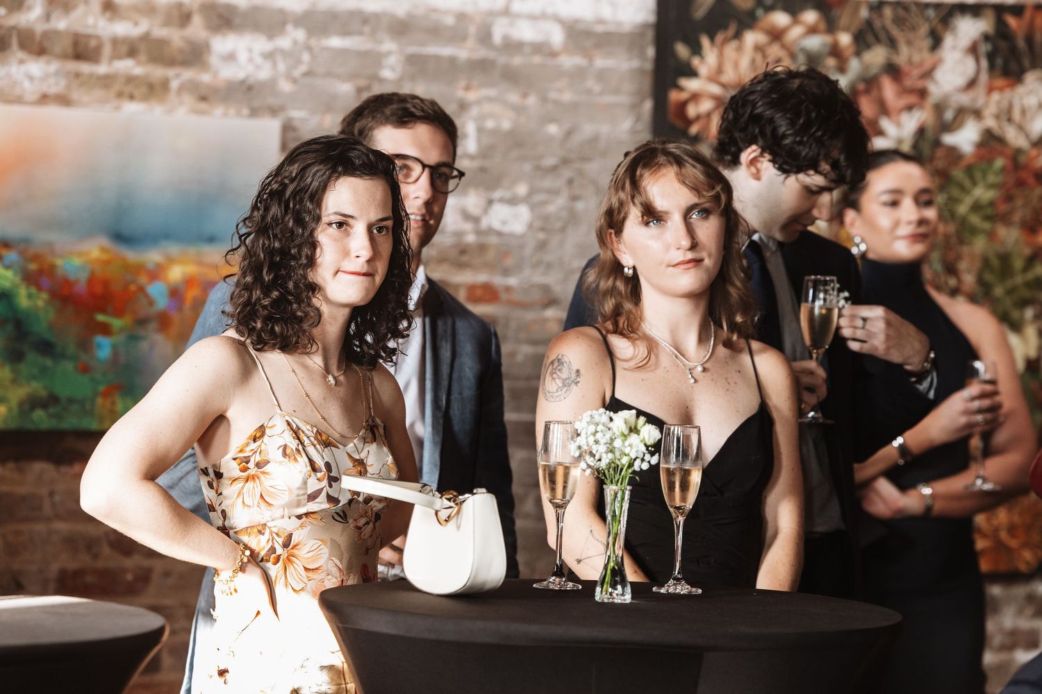 Two women and guests socializing with champagne at an elegant art gallery event.