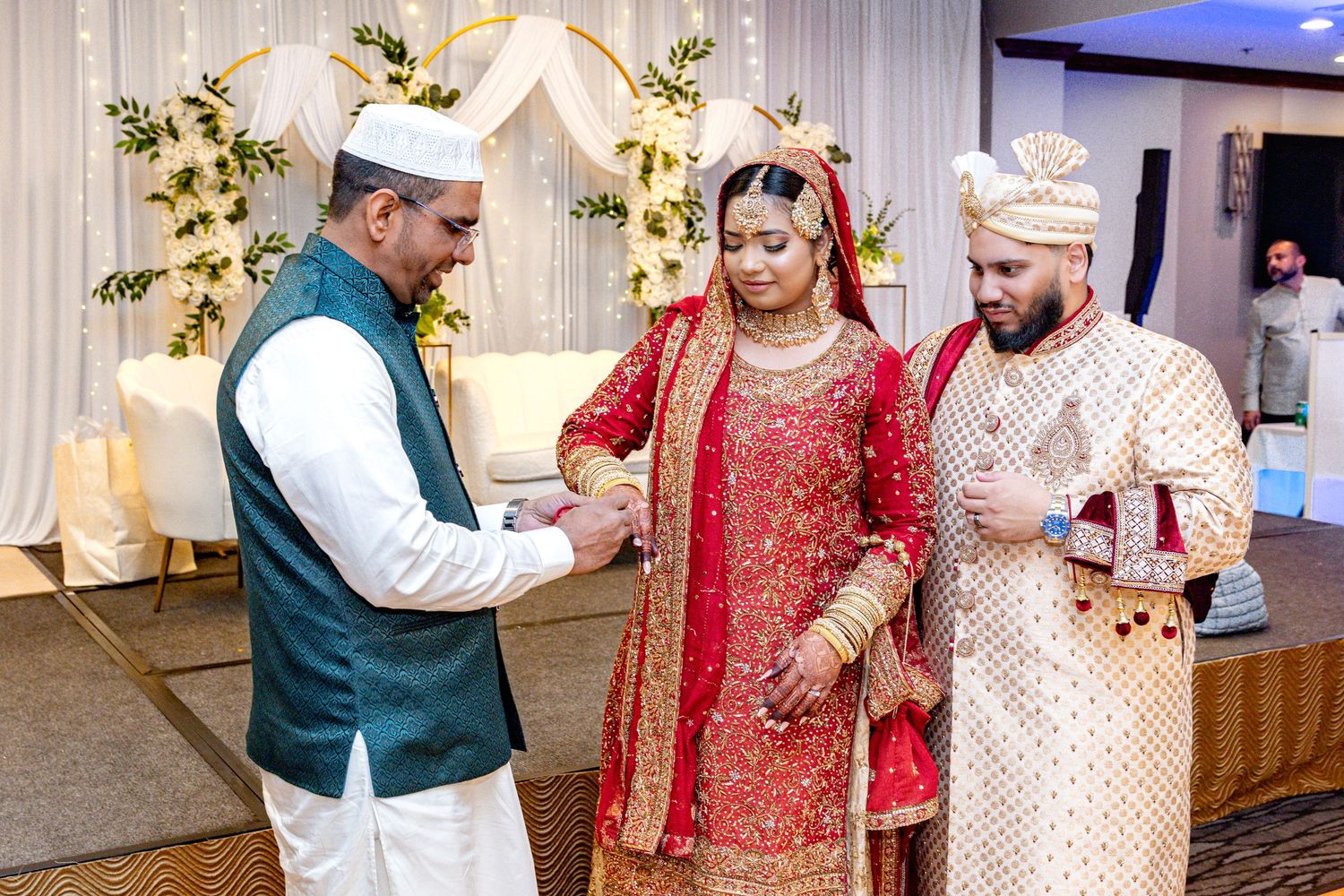 Muslim wedding ceremony with officiant blessing bride in red lehenga and groom in sherwani.