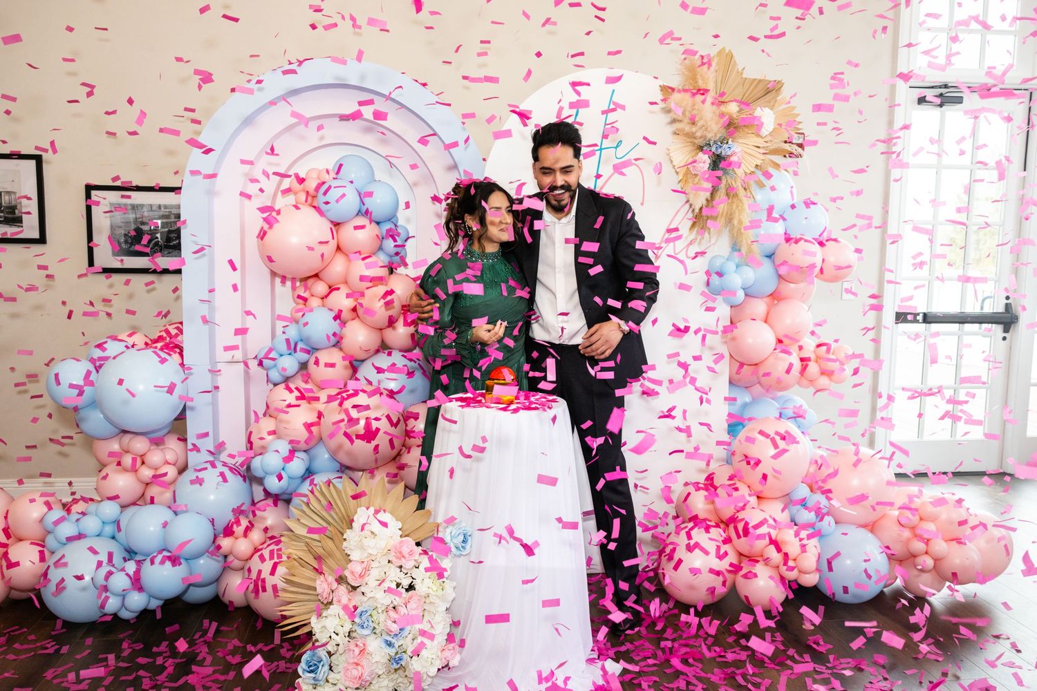 Couple cutting cake at gender reveal party with pink confetti falling around them.