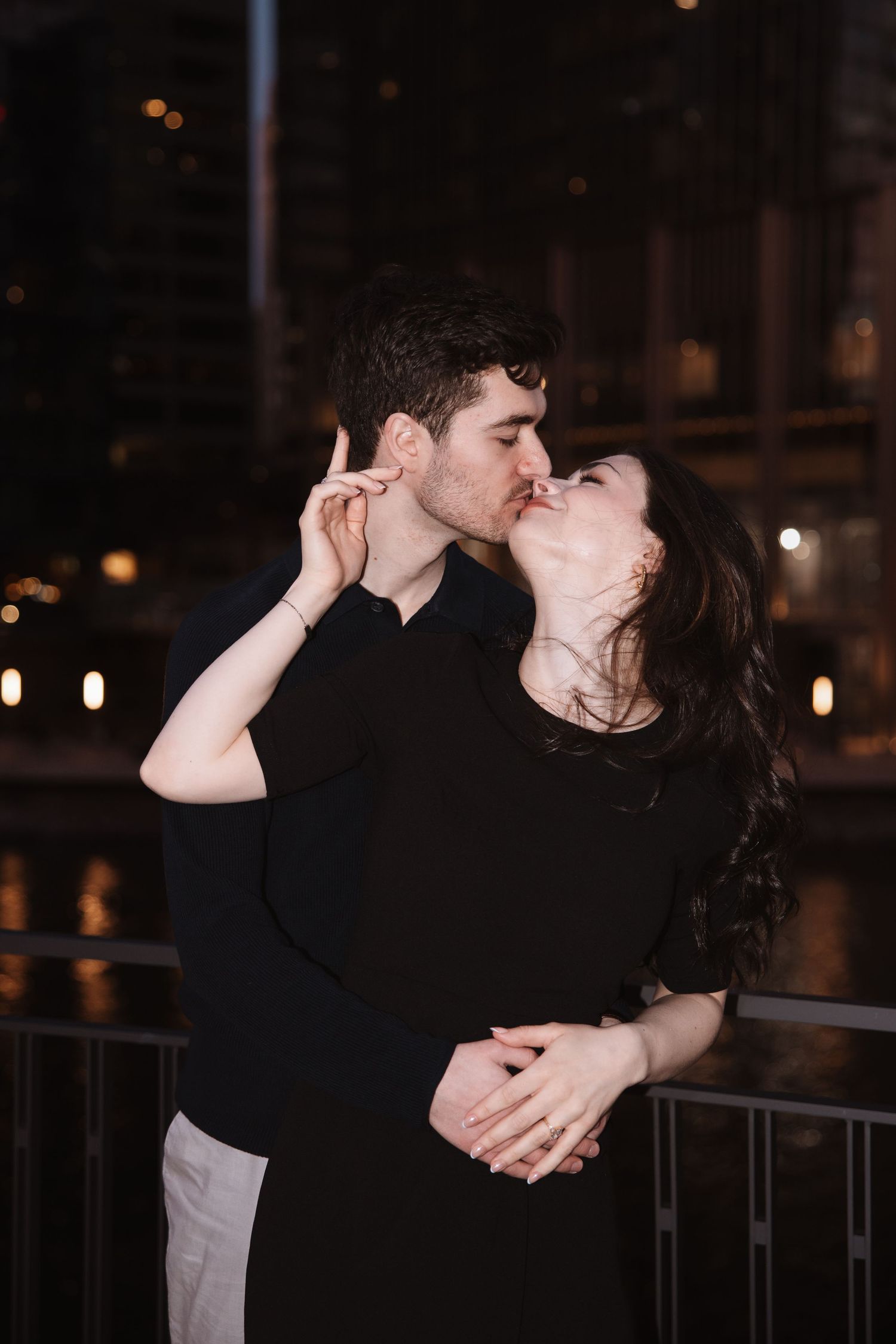 Couple kissing romantically at night with Chicago river and city lights glowing behind them.