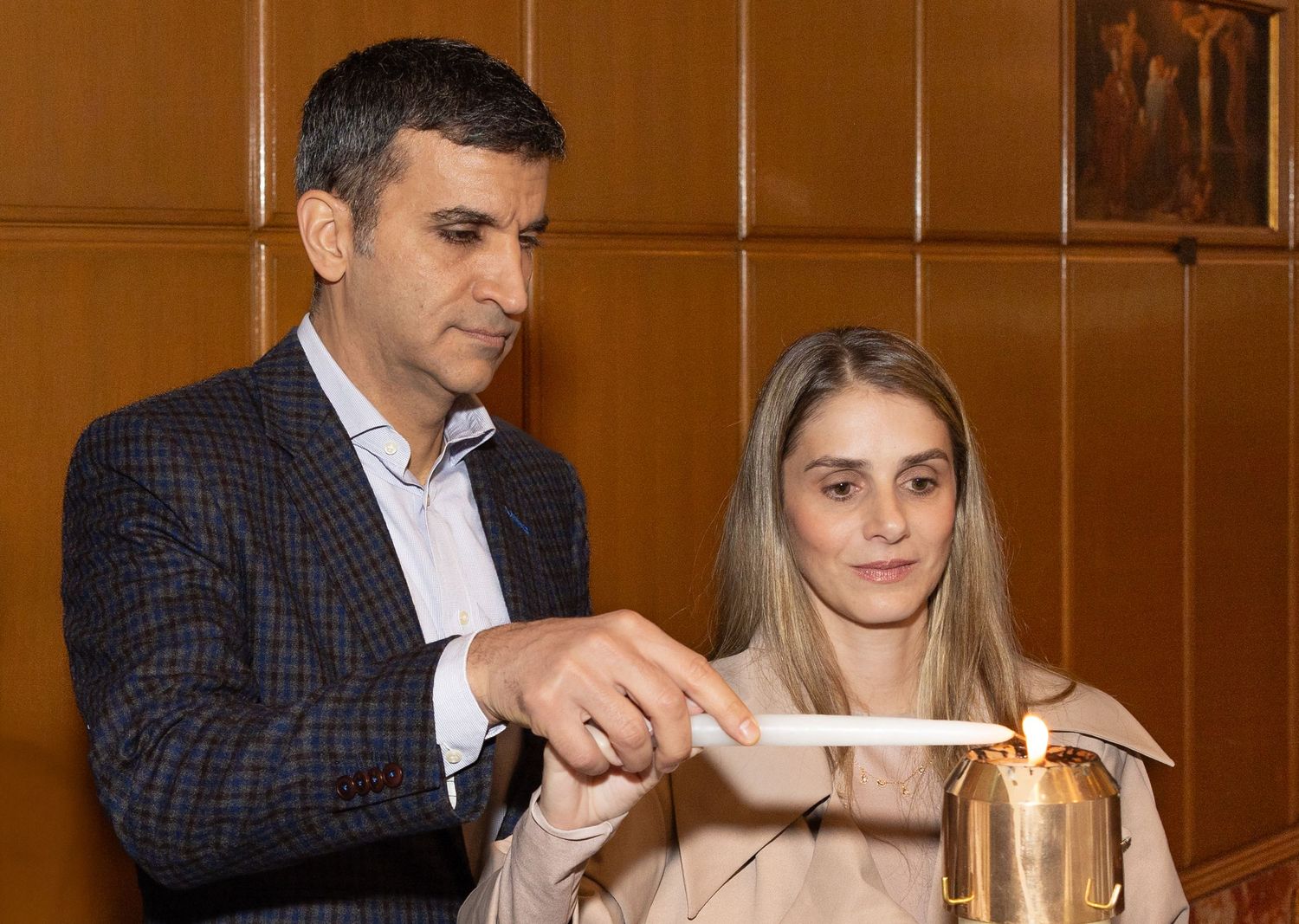Man and woman light a baptismal candle together during a christening ceremony inside a church.