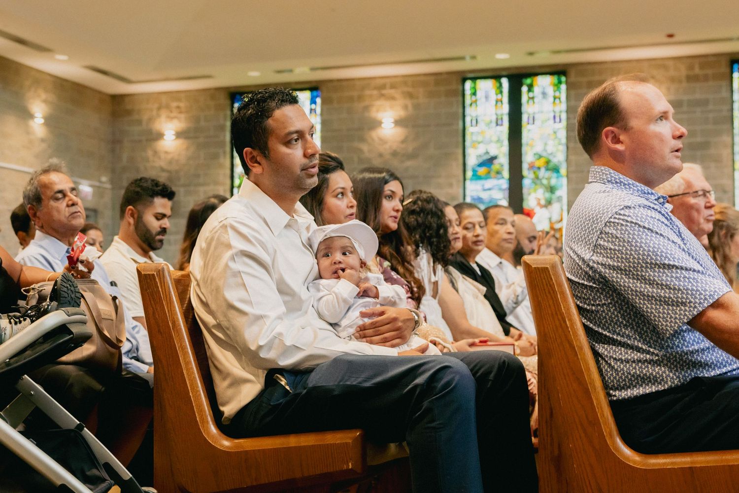 Family with baby sitting in church pews during a religious baptism ceremony.