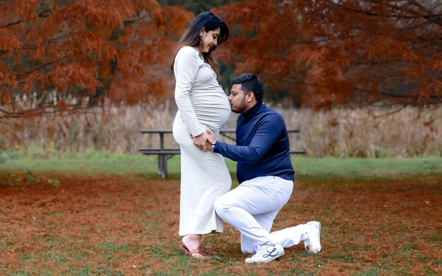 Man kneeling before pregnant partner during romantic autumn maternity photoshoot outdoors.