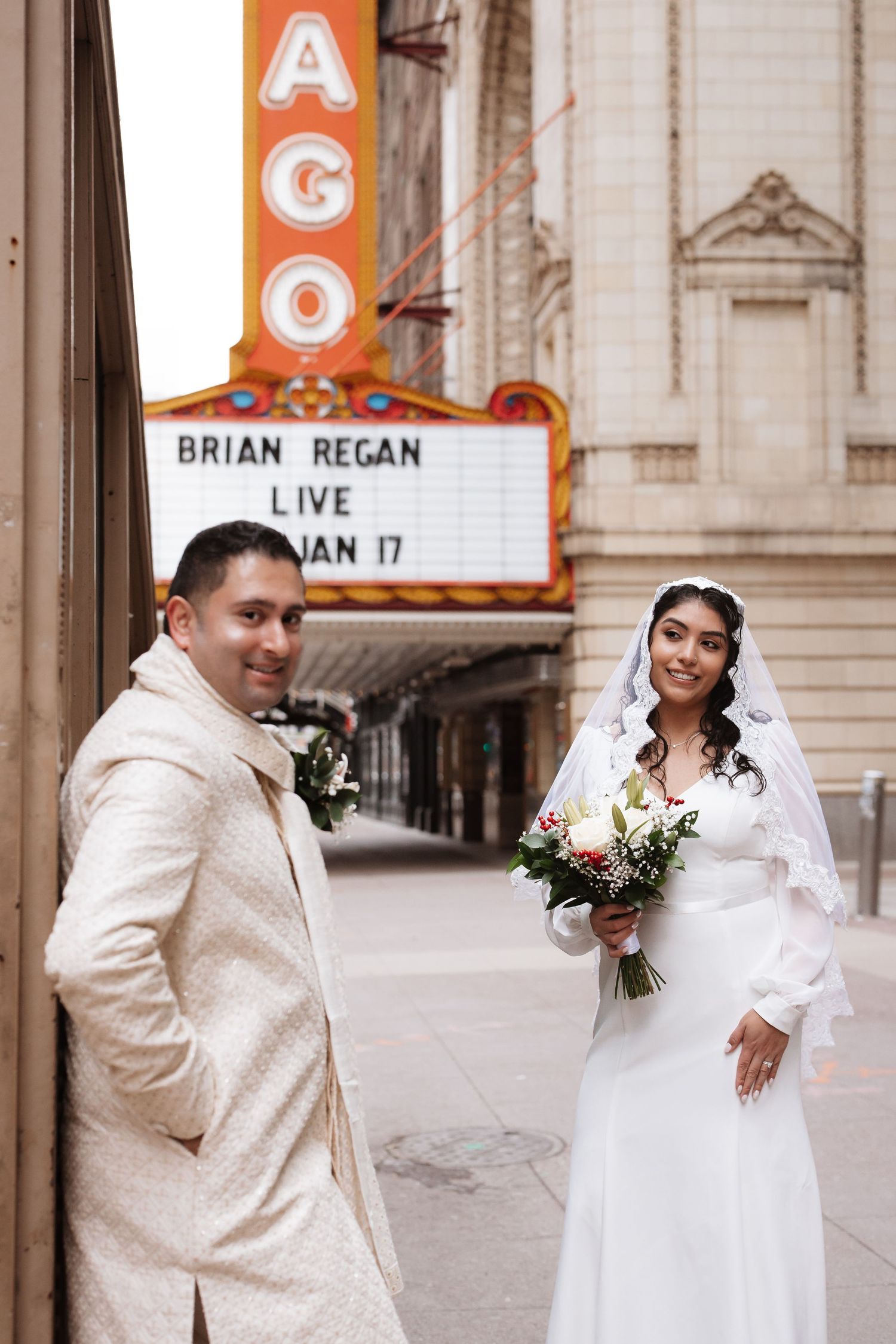 Smiling couple in wedding attire pose outside Chicago Theatre with Brian Regan marquee.