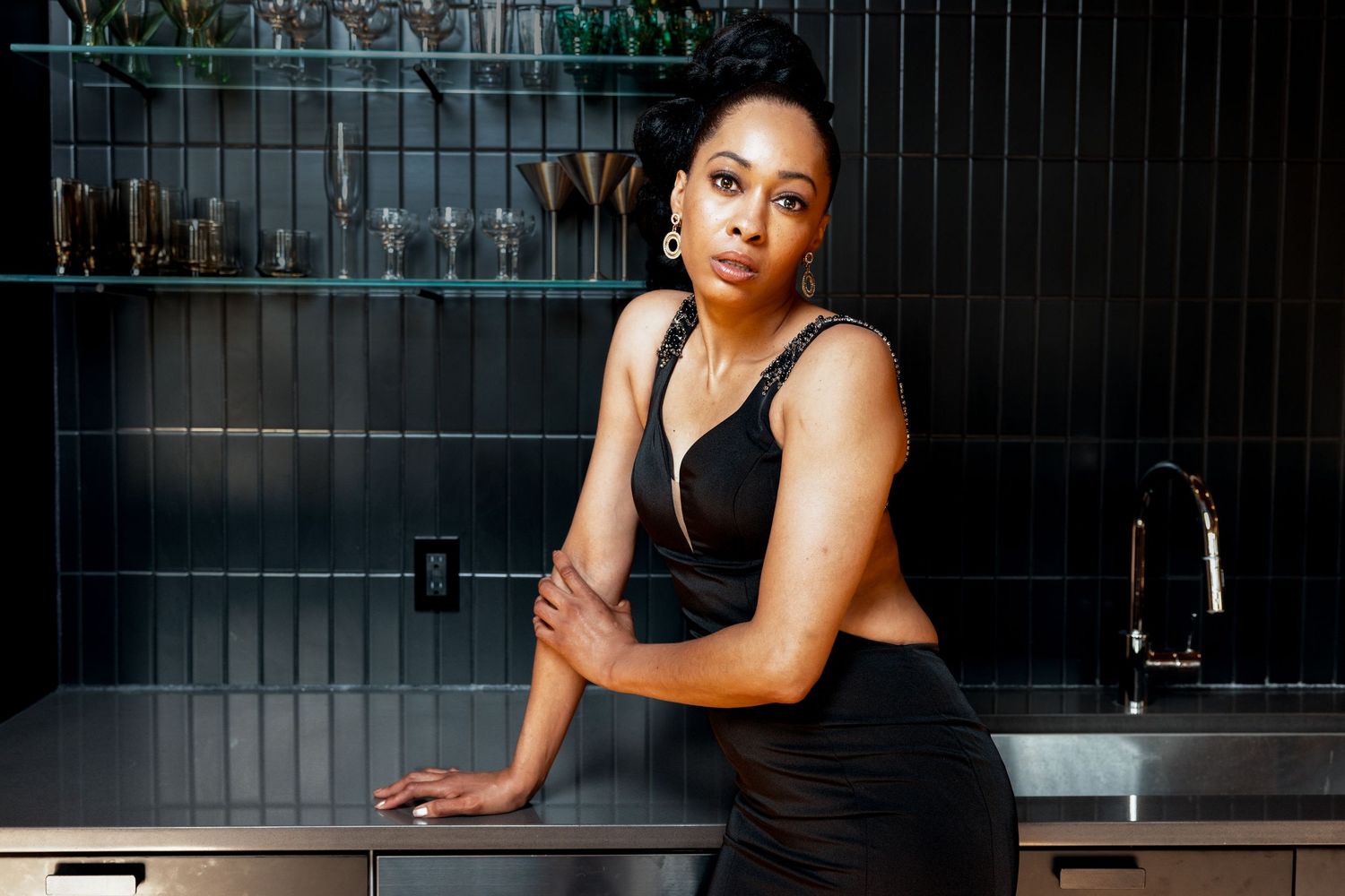 Woman in black crop top leaning on dark kitchen counter in elegant modern interior.