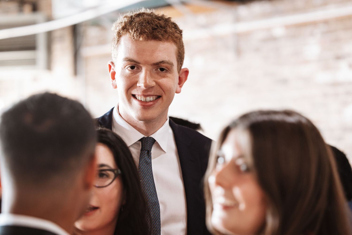 Smiling young man in dark suit and tie engages in conversation at a professional networking event.