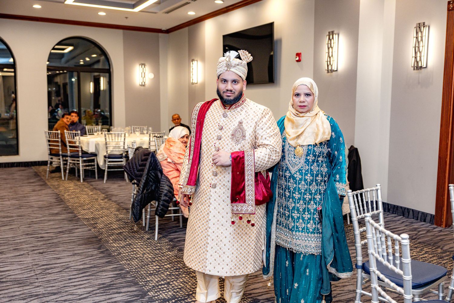 Groom in traditional sherwani and bride in blue salwar kameez posing at South Asian wedding venue.
