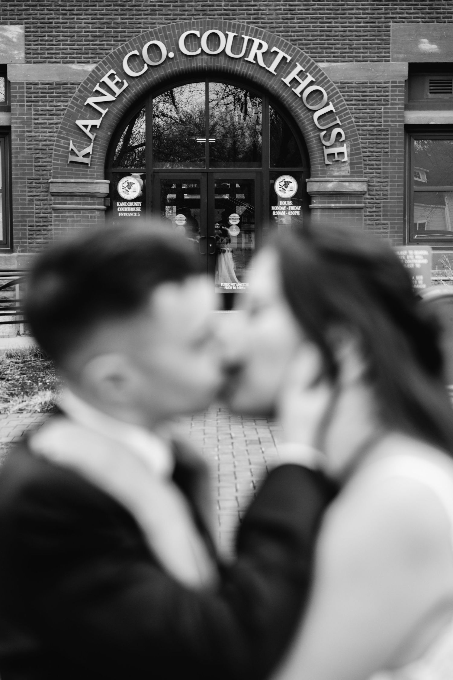 Black and white photo of couple kissing in front of Kane Co. Courthouse on their wedding day.