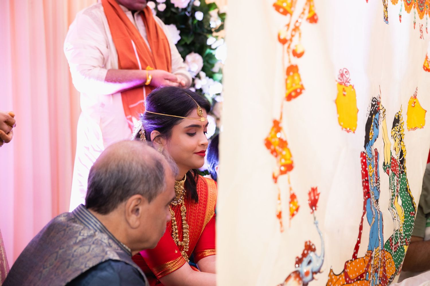 Hindu bride in red saree with gold jewelry bowing during traditional wedding ceremony blessing ritual.