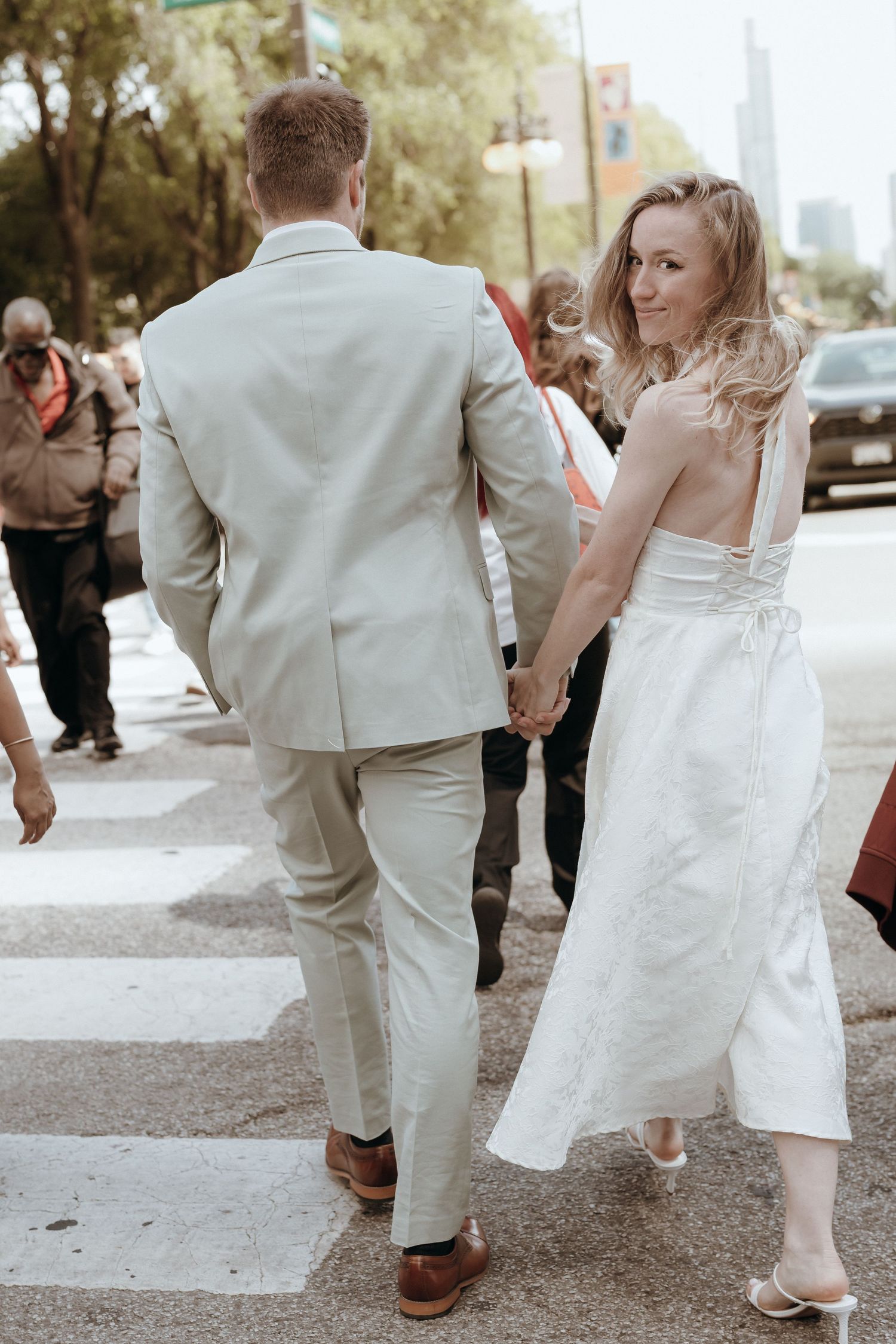 Bride and groom walk hand-in-hand across a crosswalk, bride glancing back over her shoulder.