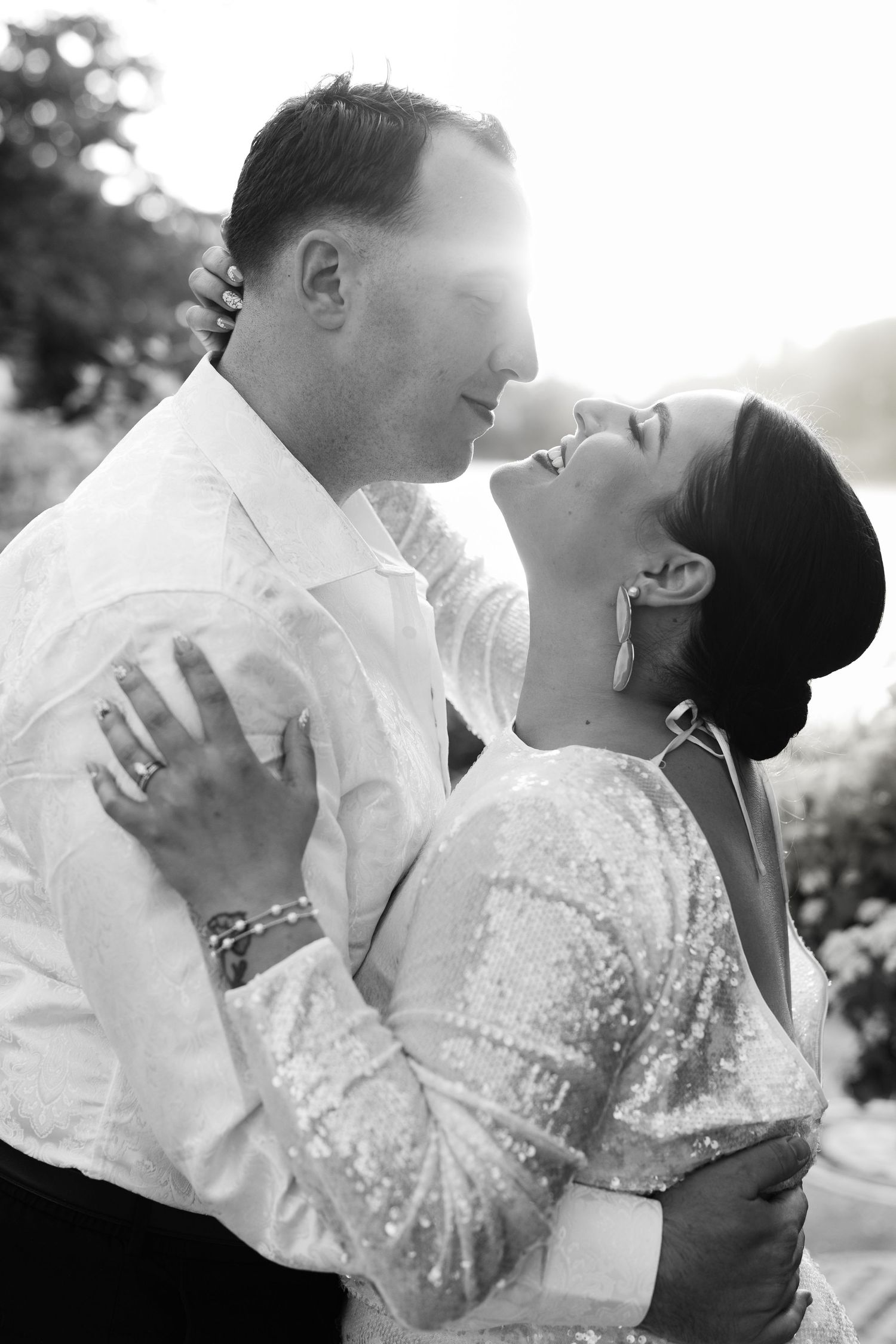 Black and white photo of bride and groom sharing romantic moment outdoors in sunlight.