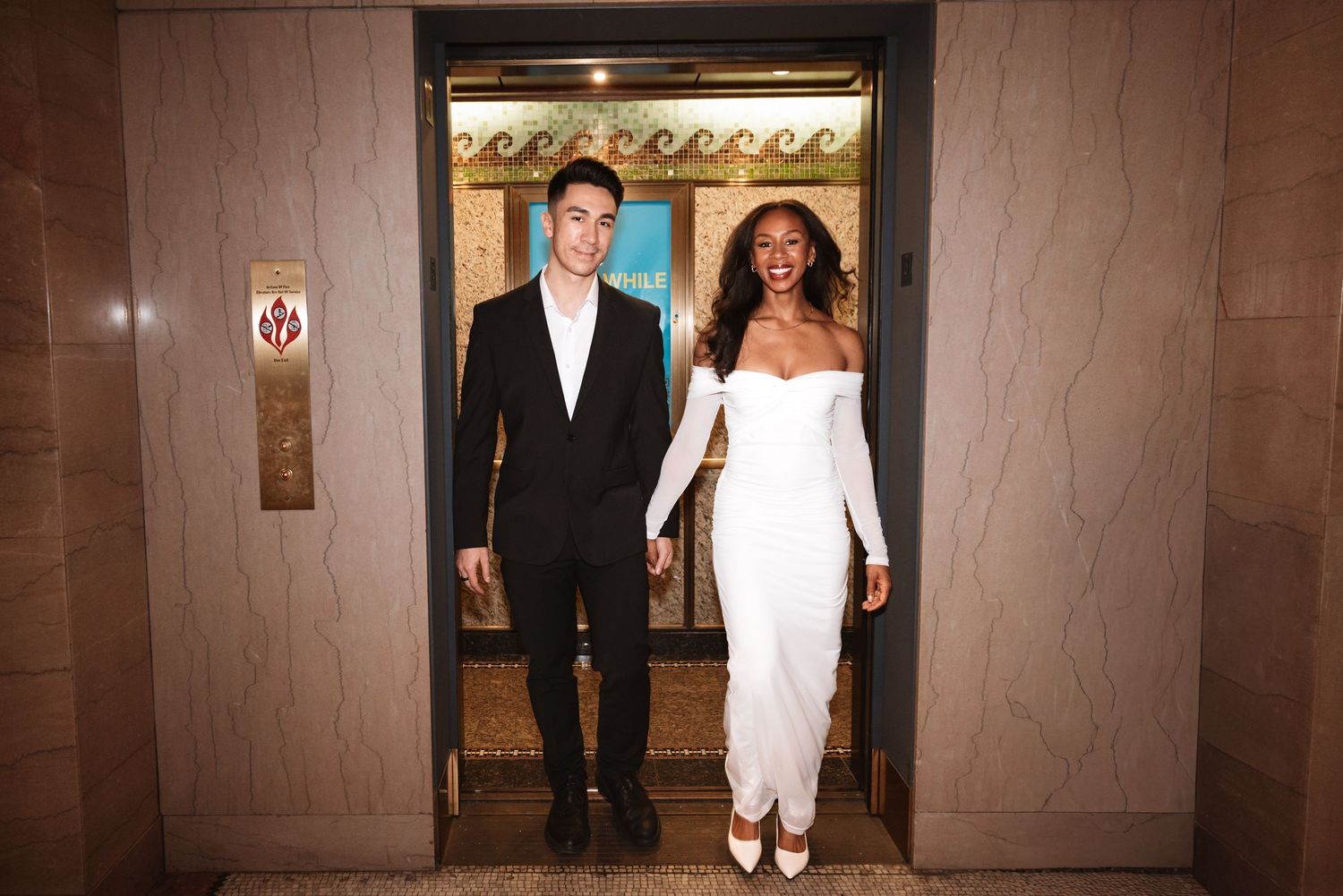 Smiling newlywed couple walking out of an ornate elevator, bride in white gown and groom in black suit.Chicago Wedding Photographer
