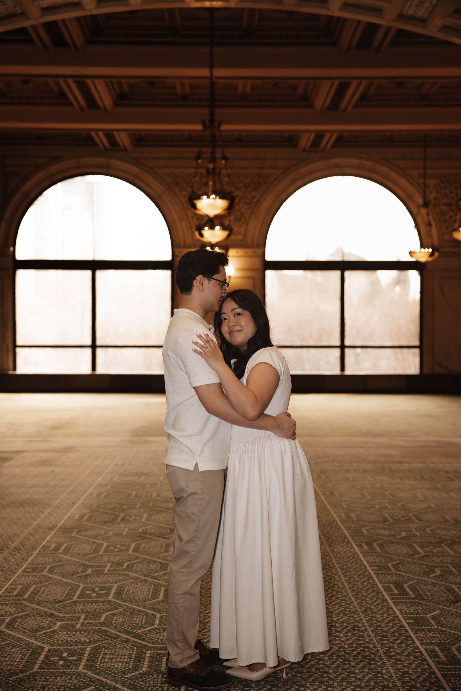 Engaged couple embraces in warm golden light inside the arched hall of the Chicago Cultural Center.