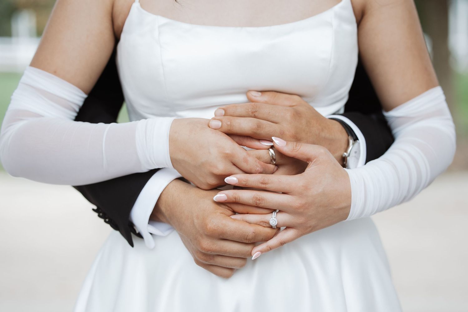 Bride and groom holding hands showing wedding rings, bride wearing white dress and gloves.