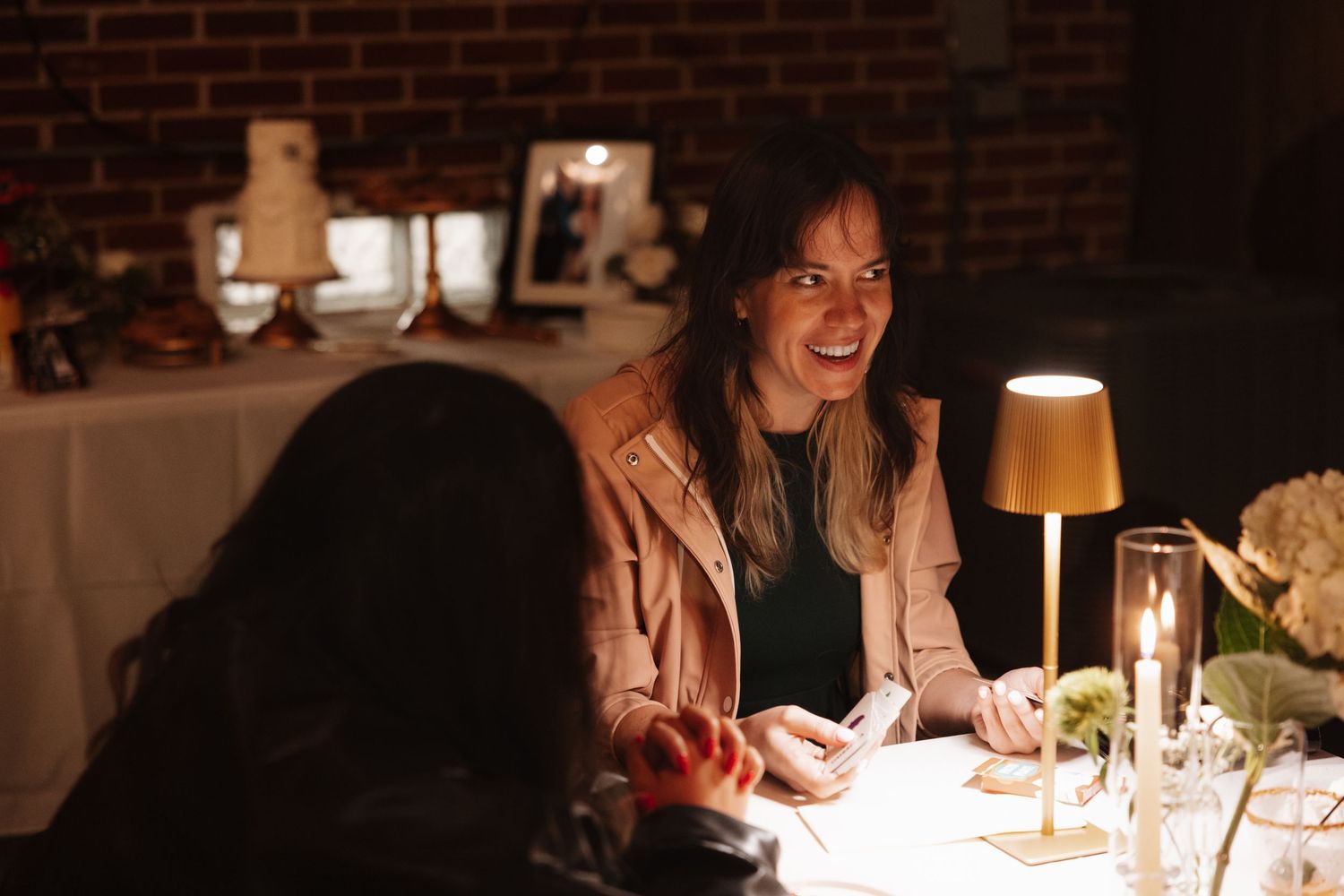 Woman smiling warmly at candlelit wedding reception dinner table in dimly lit venue.