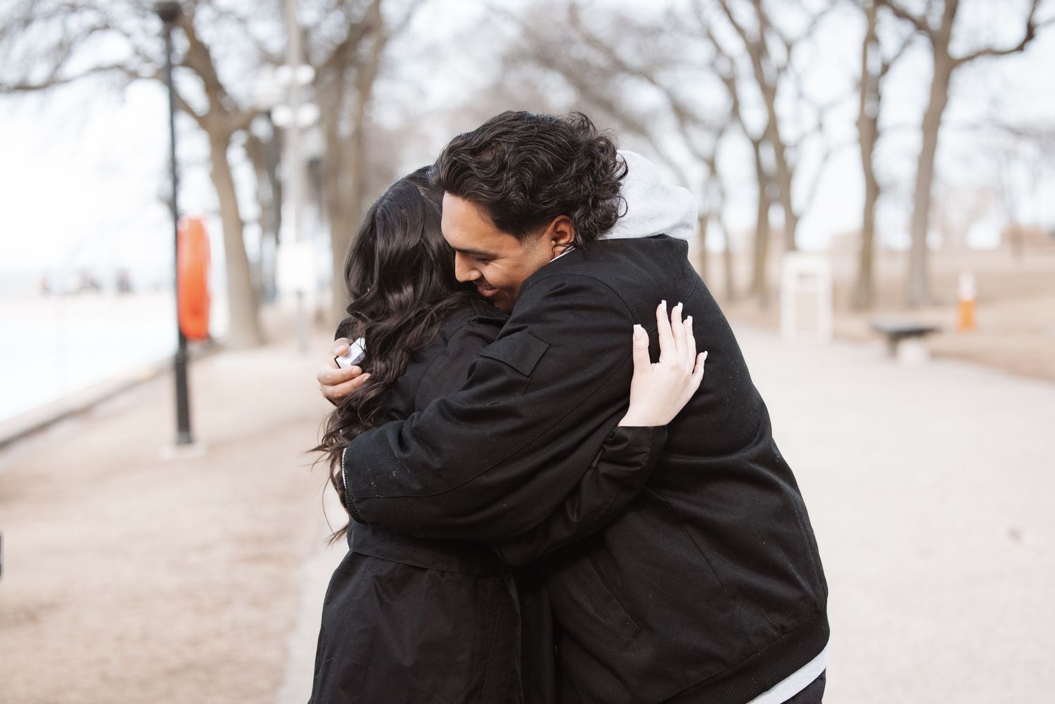 Couple sharing a warm embrace on a tree-lined path in a Chicago park during winter.