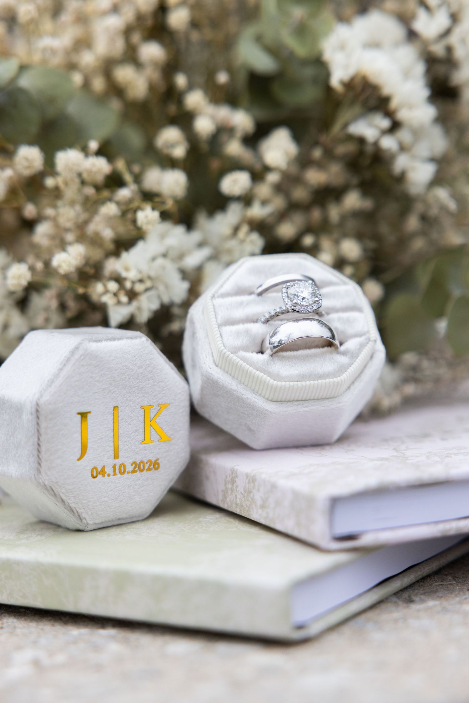 White velvet octagonal ring box monogrammed J|K with wedding date 04.10.2026, holding diamond engagement and wedding bands.