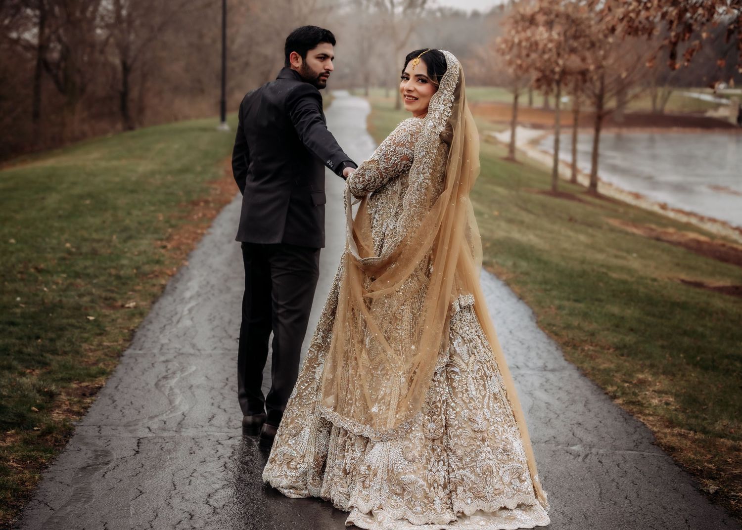 South Asian couple on rainy day, groom in black suit, bride in gold embroidered bridal lehenga.