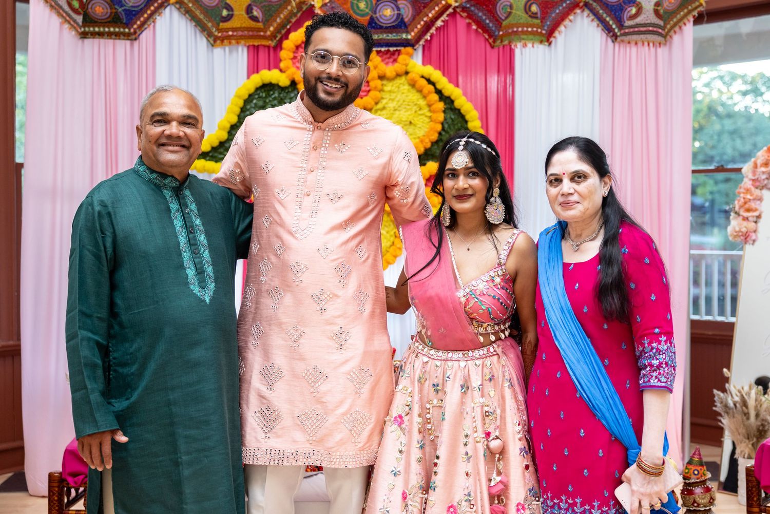 Indian family of four poses together in traditional attire at colorful wedding ceremony.