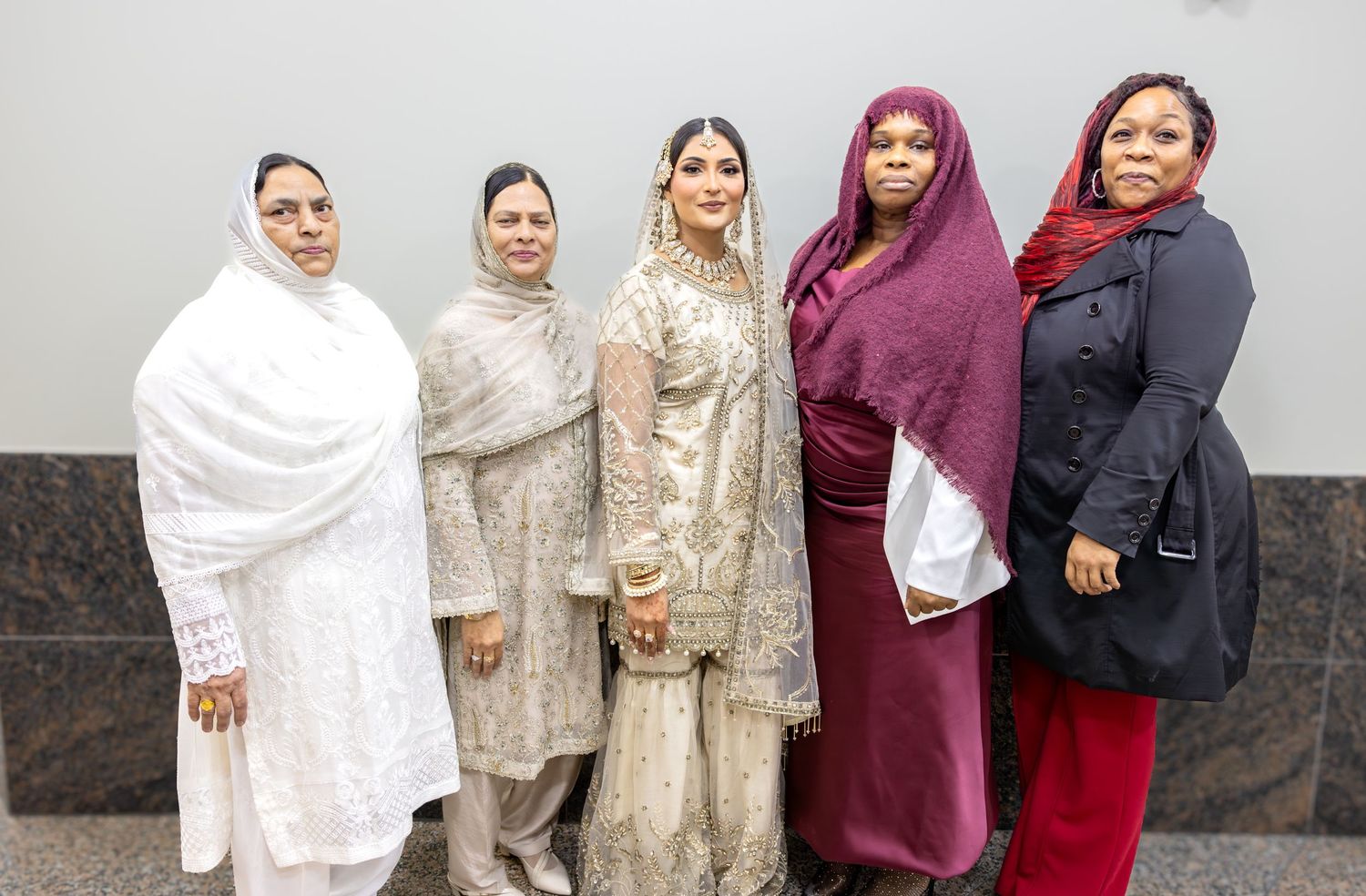 Muslim bride in white lehenga poses with four female family members in hijabs at wedding ceremony.