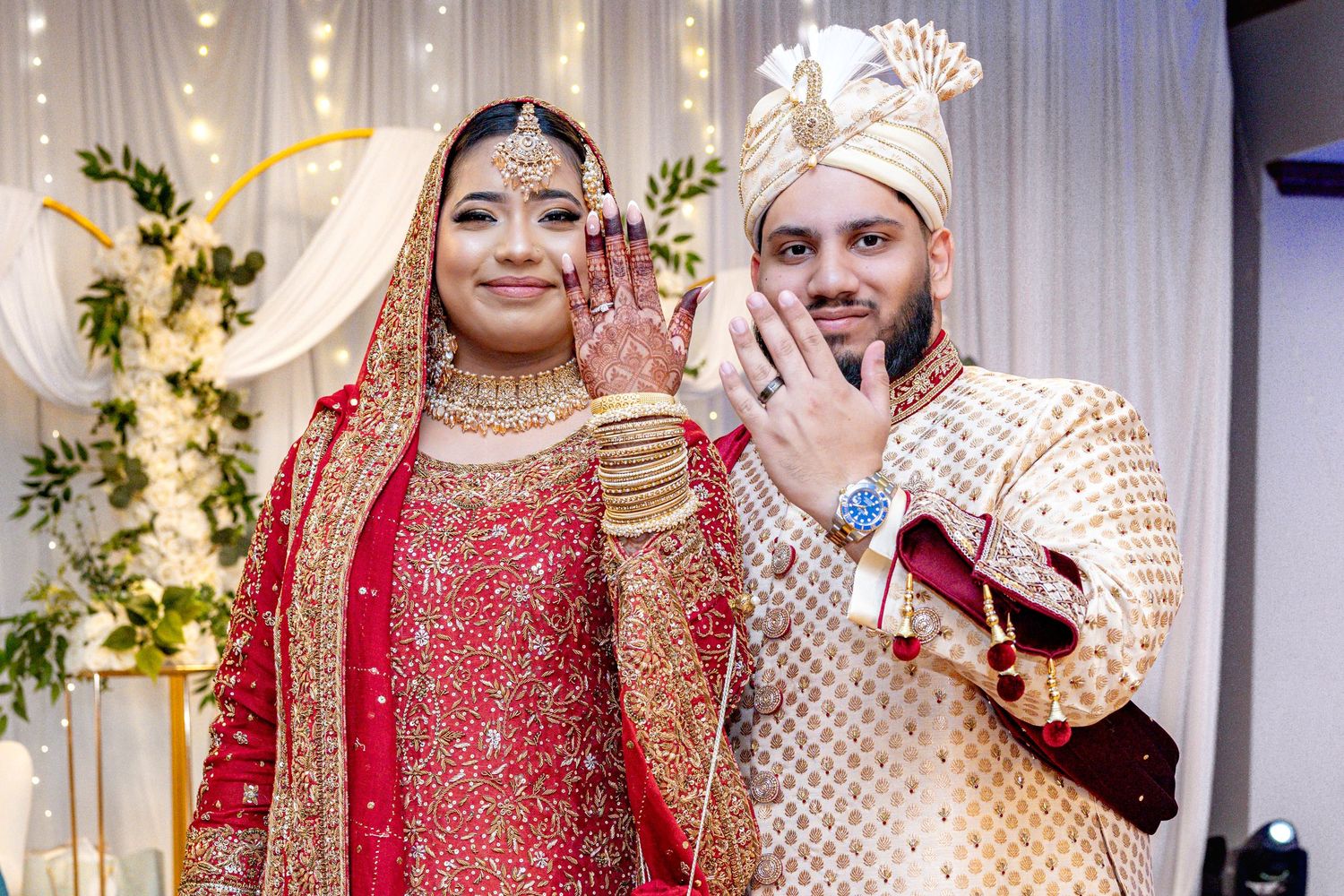 South Asian bride and groom showing rings in traditional wedding attire.