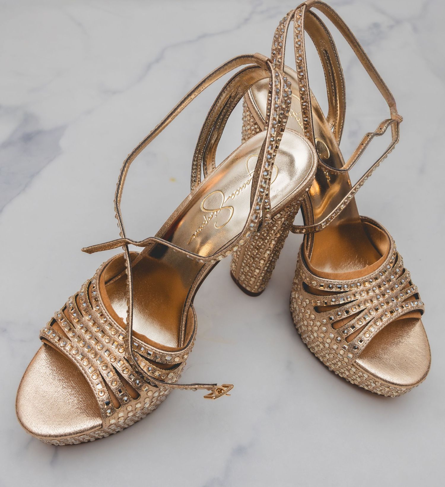 Gold crystal-embellished strappy block heel wedding shoes on marble surface.