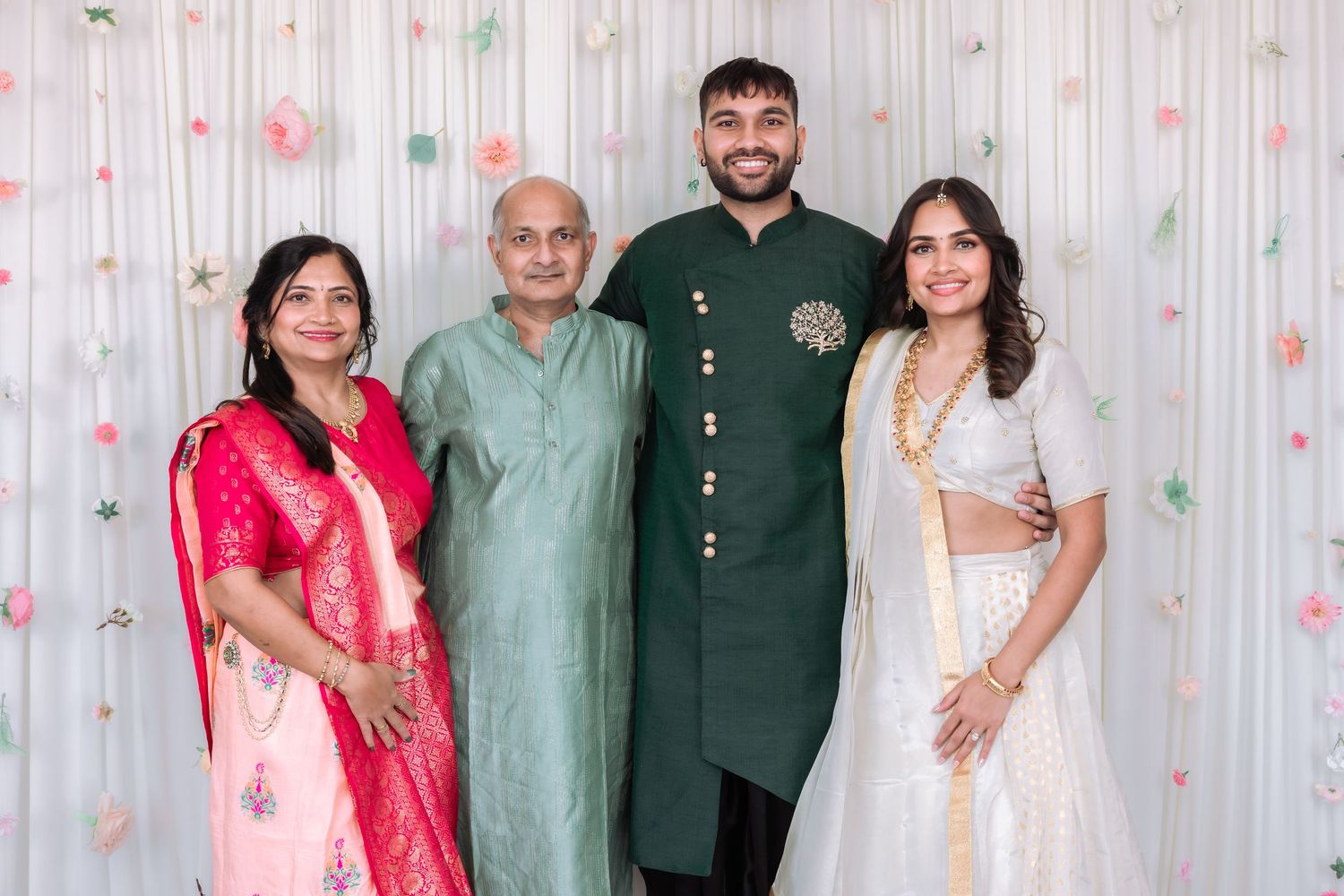 Indian family portrait at engagement celebration with traditional attire and floral backdrop.