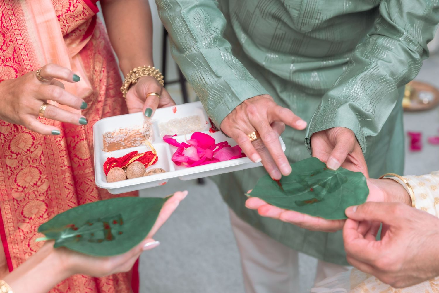 Hands holding green betel leaves and a tray with rose petals during a traditional Hindu wedding ceremony.