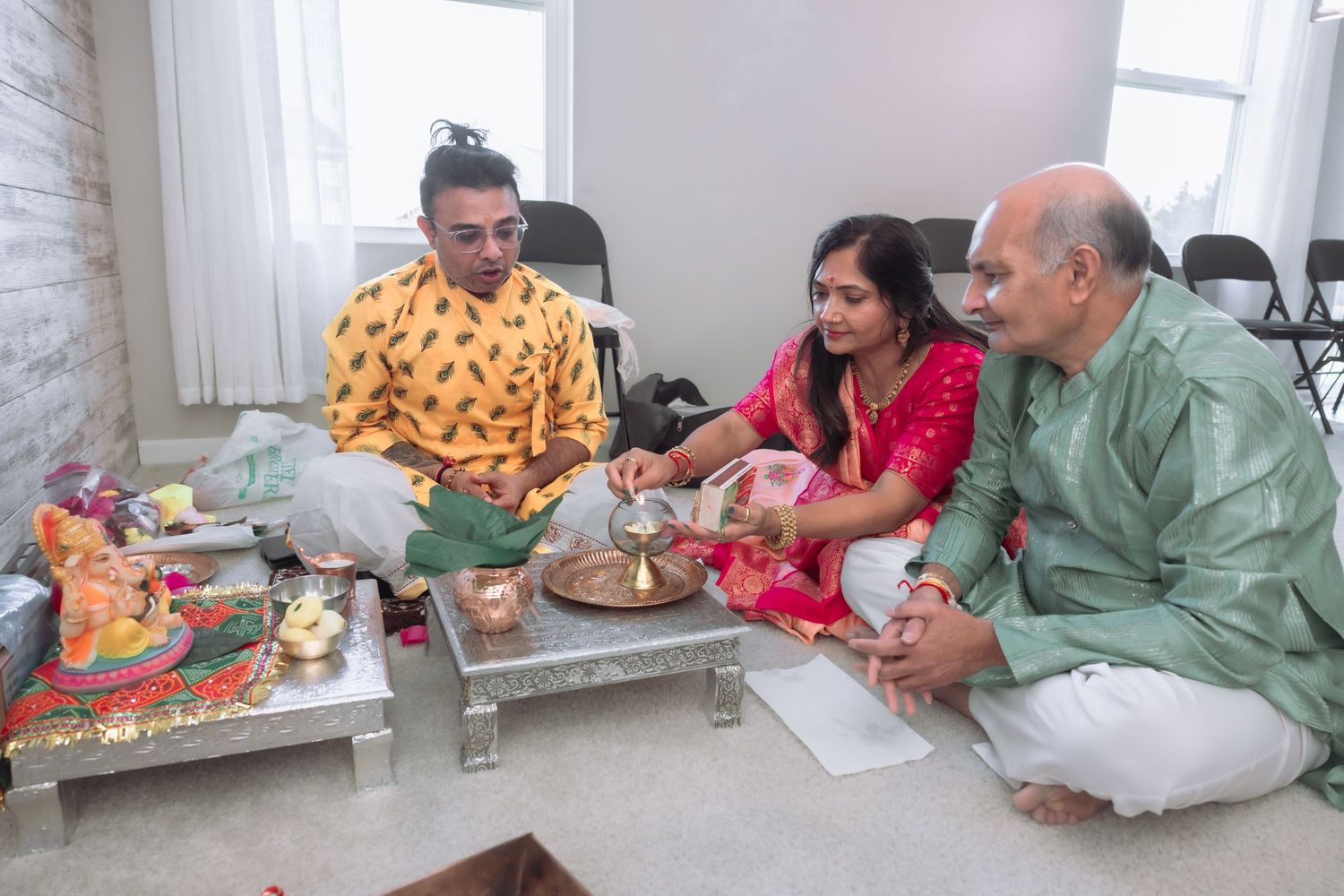 Indian family performing Hindu puja ritual seated on floor with priest and ceremonial items.