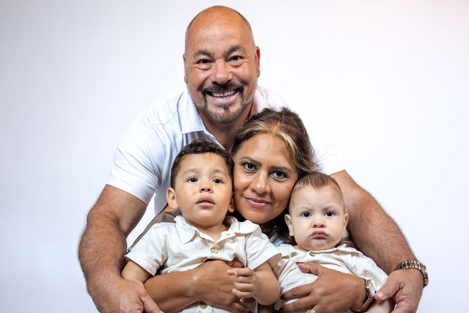 Happy family portrait of parents with two young babies dressed in matching outfits on white background.