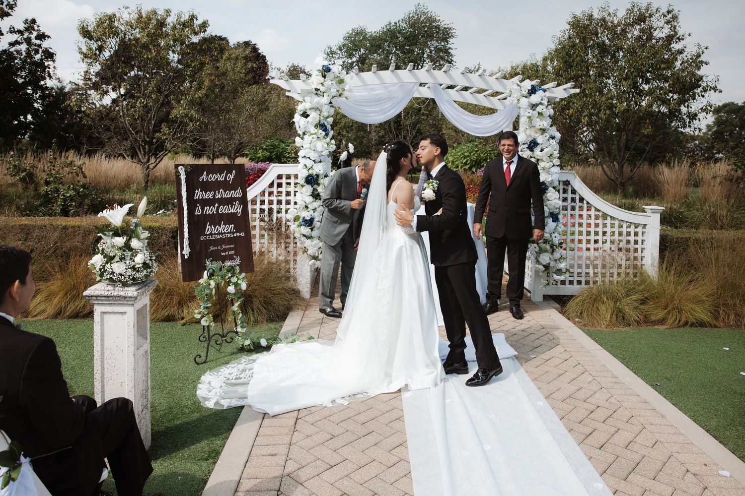 Bride and groom stand together at white lattice arch during elegant outdoor wedding ceremony.