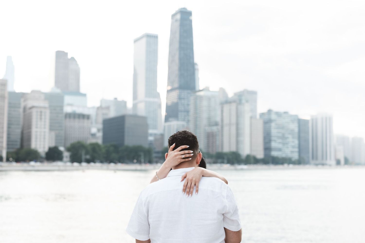 Couple embracing with backs turned, overlooking Chicago skyline and lakefront on a cloudy day.