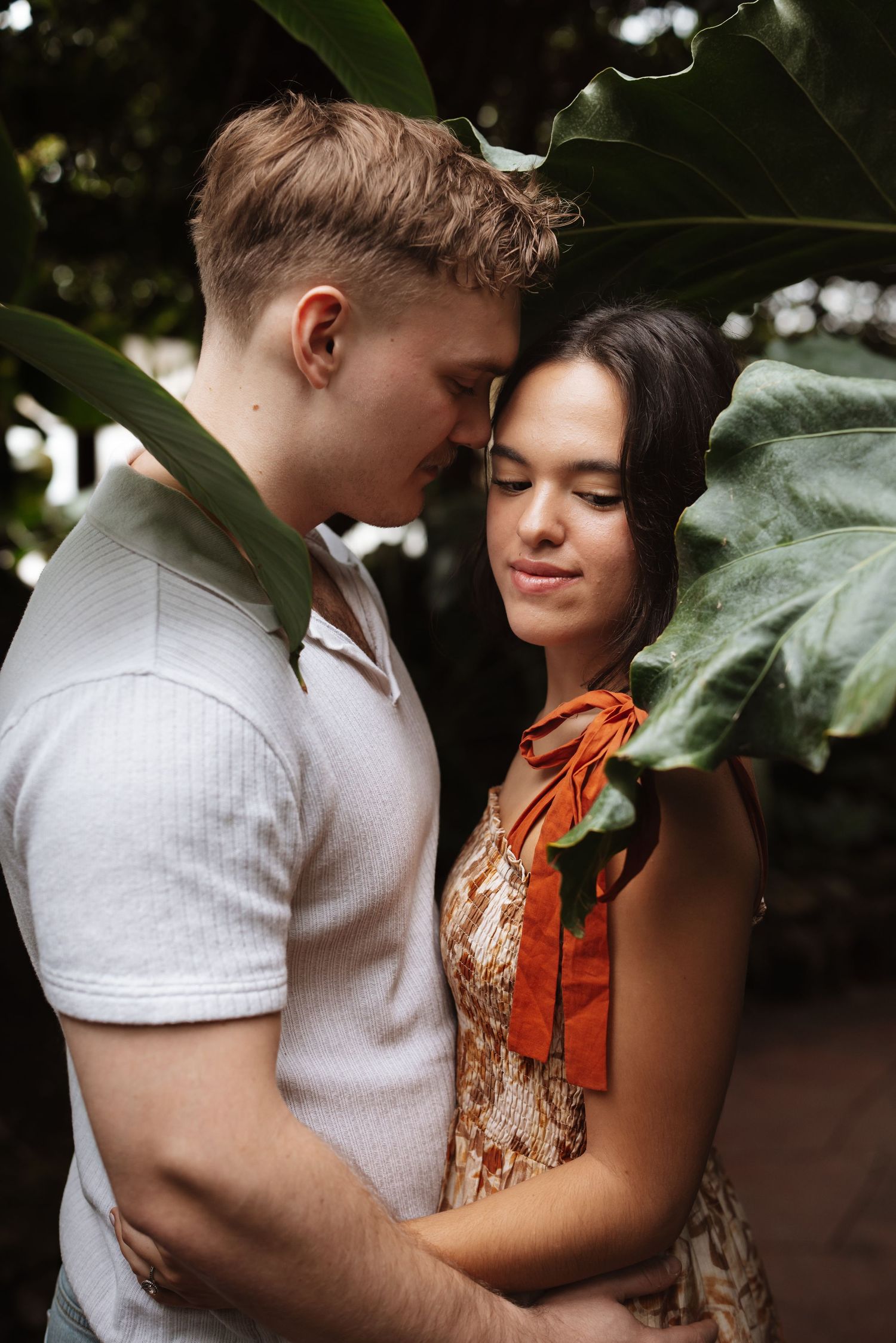 Romantic couple embracing tenderly among lush tropical green leaves in a garden setting.