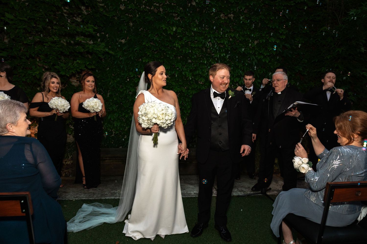 Bride and groom smile while walking back down aisle after outdoor wedding ceremony.