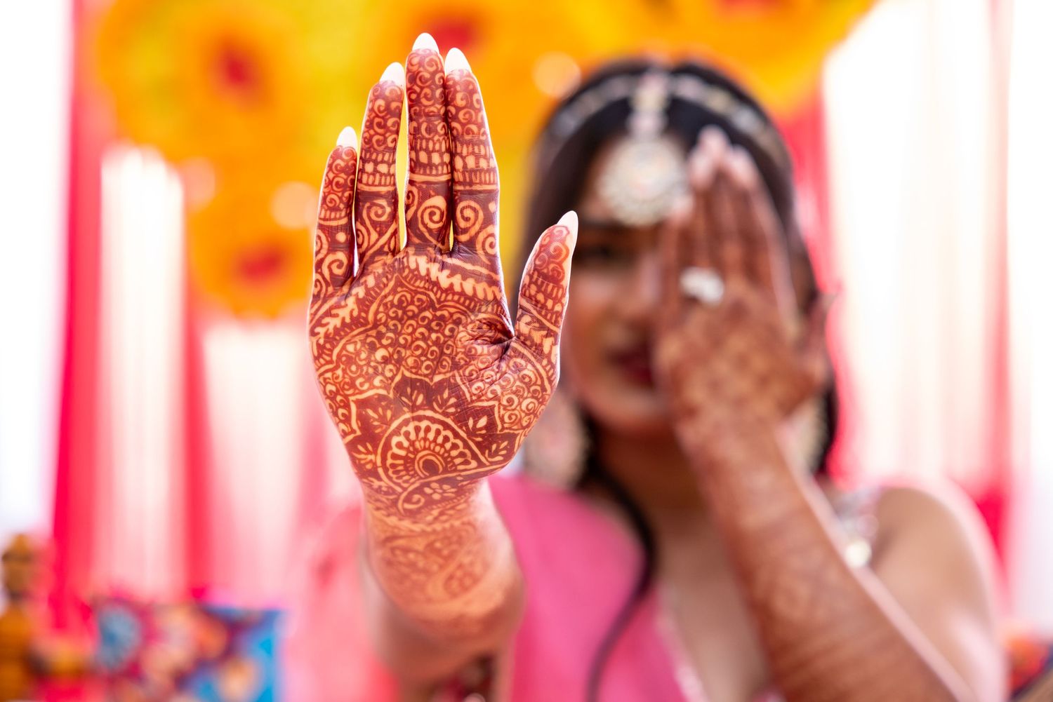 Indian bride displaying intricate henna mehndi design on raised palm at ceremony.